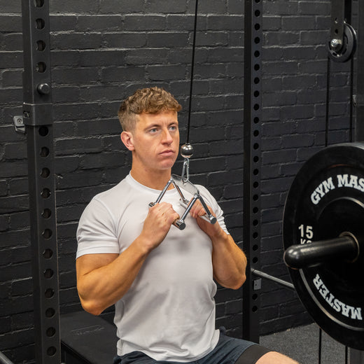Angled shot of man performing excersises with cable crossover machine stirrup attachment in gym background